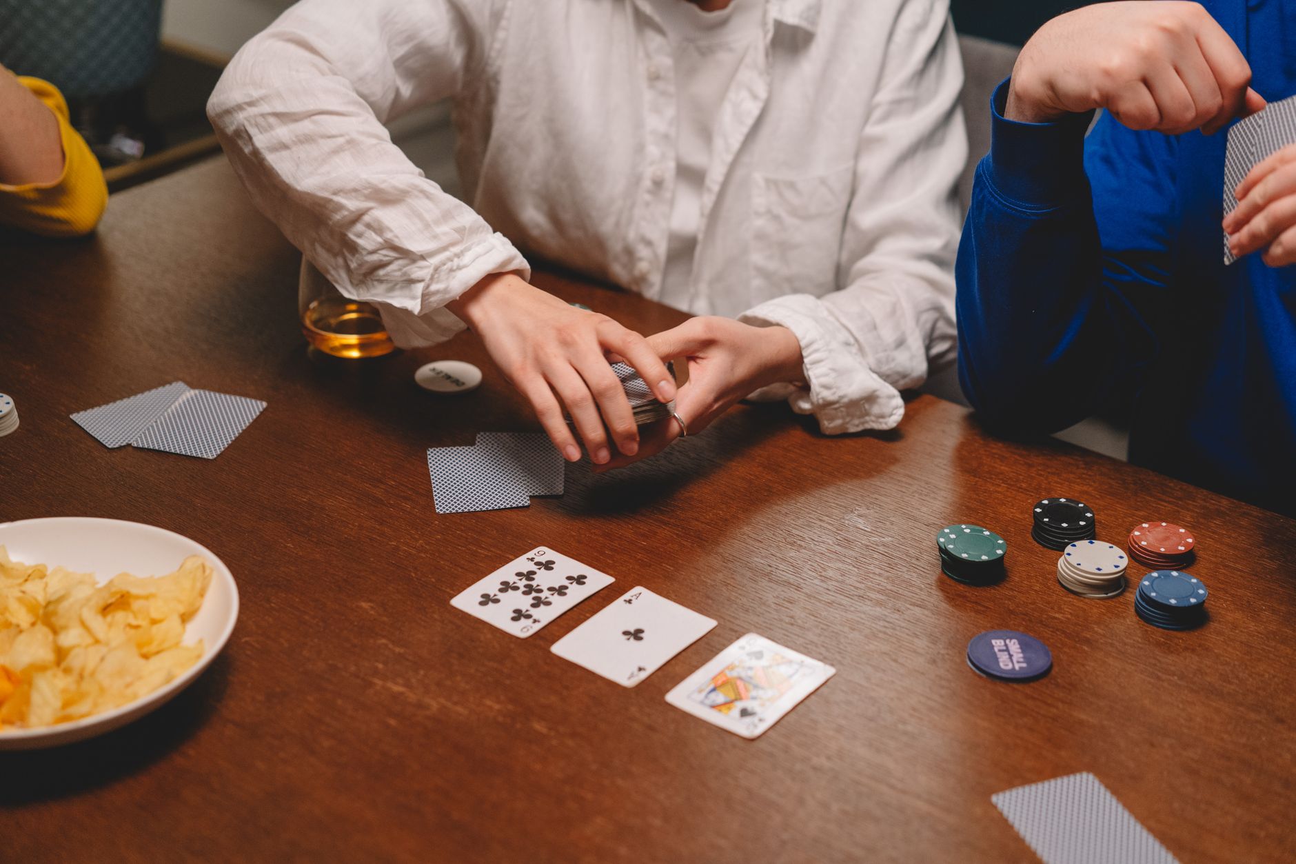 Un groupe de personnes participant à une partie de poker informelle avec des jetons et des cartes sur une table en bois.