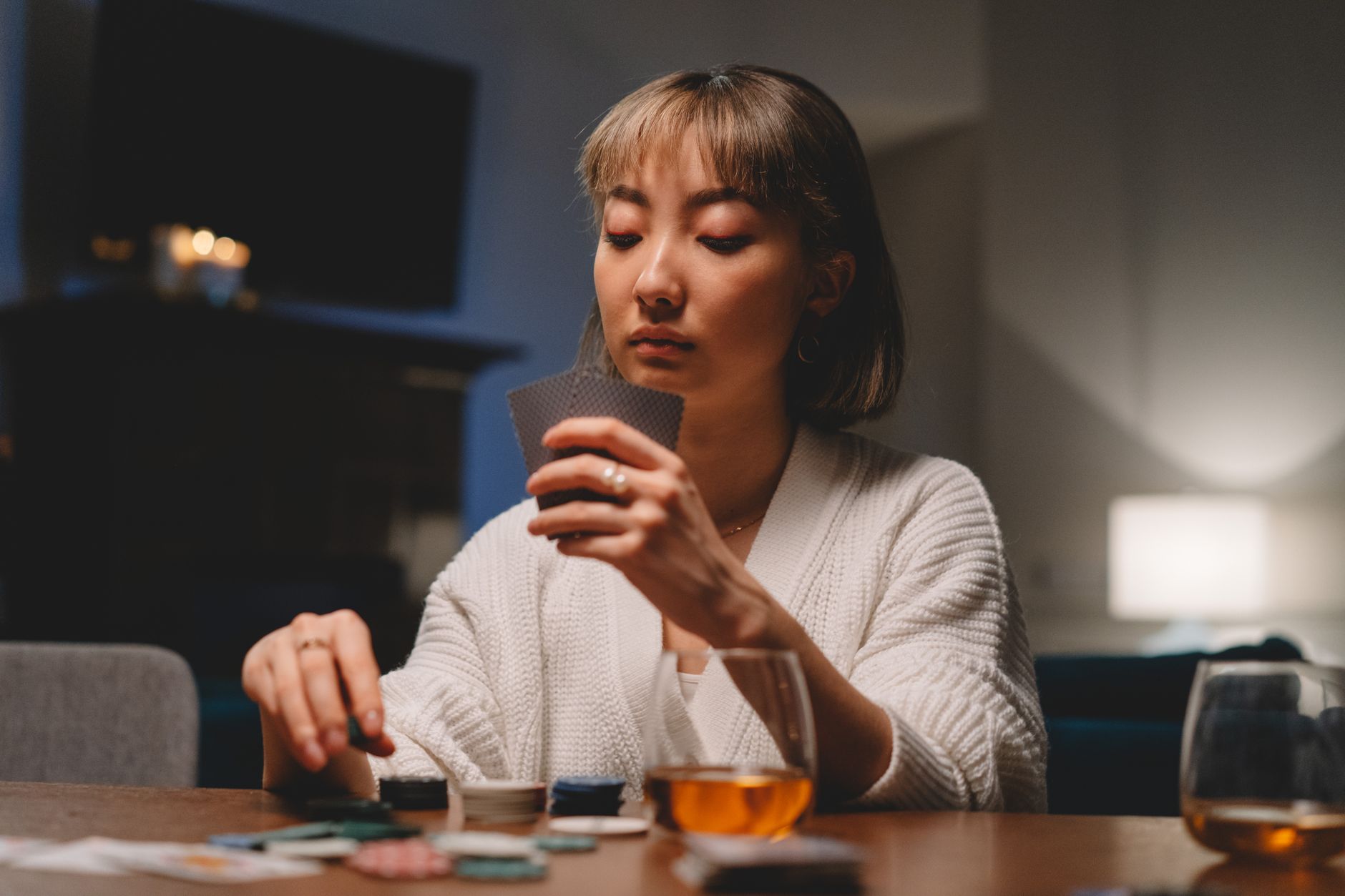 Une femme dans un cadre confortable, sérieusement engagée dans une partie de poker avec des cartes et des jetons sur la table.
