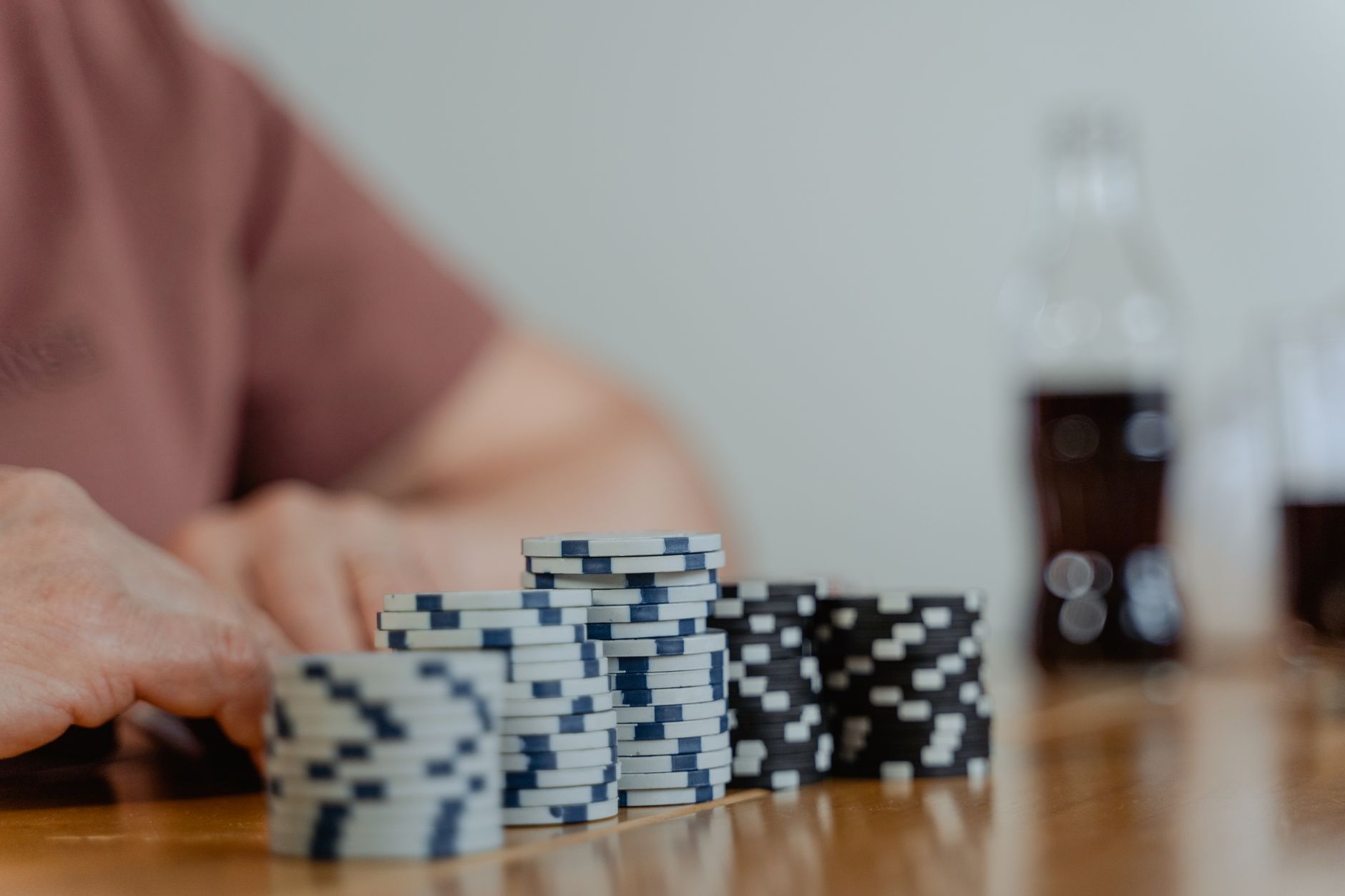 Piles de jetons de poker blancs et noirs sur une table en bois, avec une personne floue aux mains posées près des jetons.