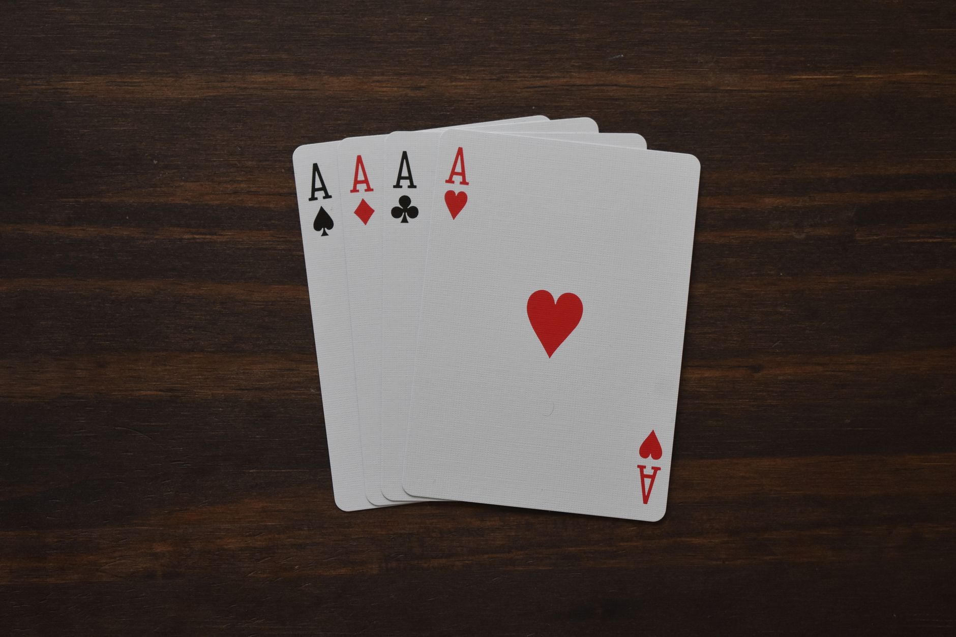 Quatre as de pique, carreau, trèfle et cœur disposés en éventail sur une table en bois sombre.